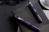 Purple pen and glasses on a black desk with a notebook