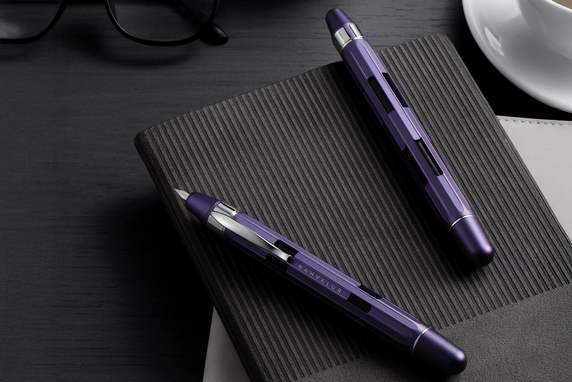 Purple pen and glasses on a black desk with a notebook