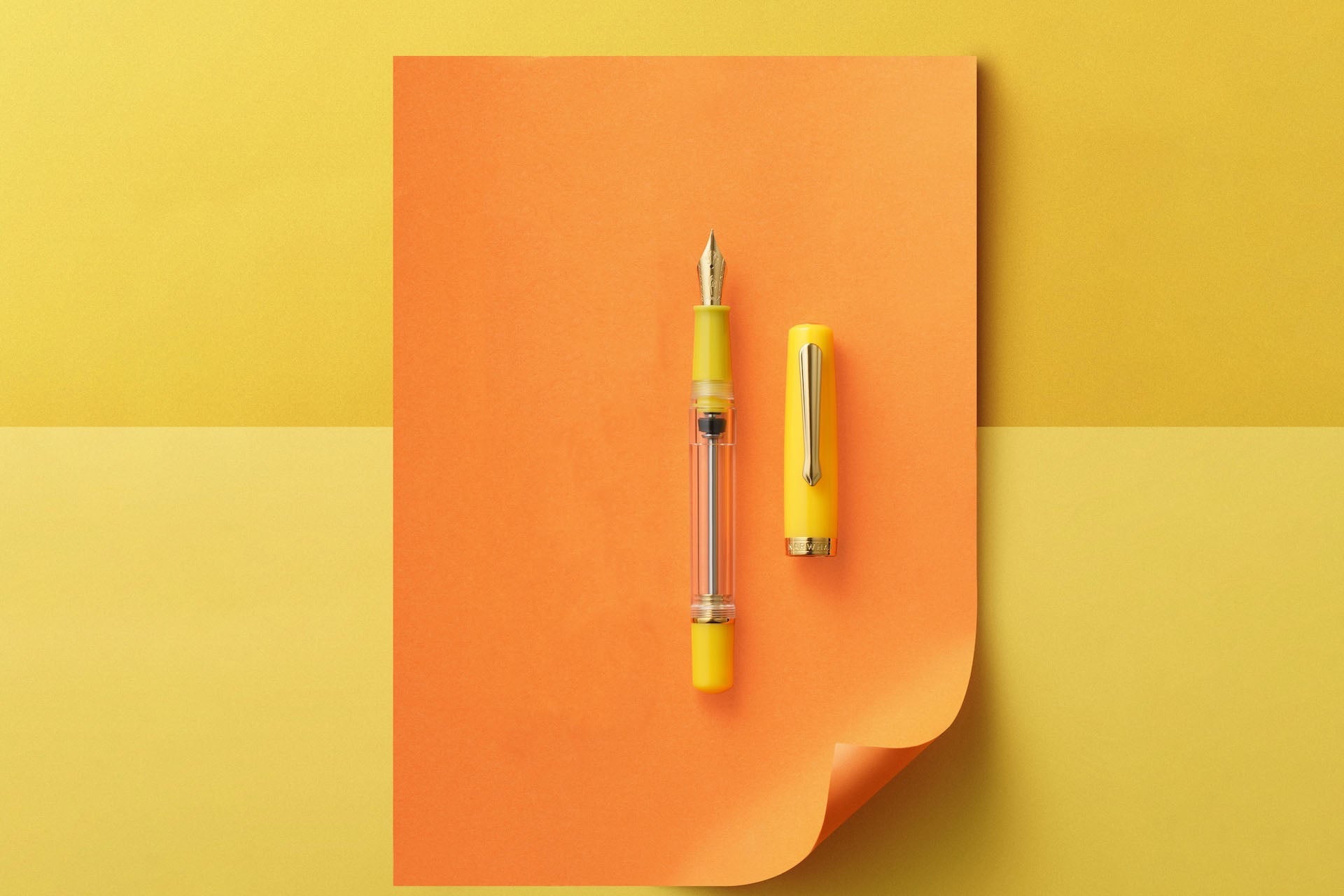 Yellow pen and its cap on an orange notebook against a two-tone yellow background